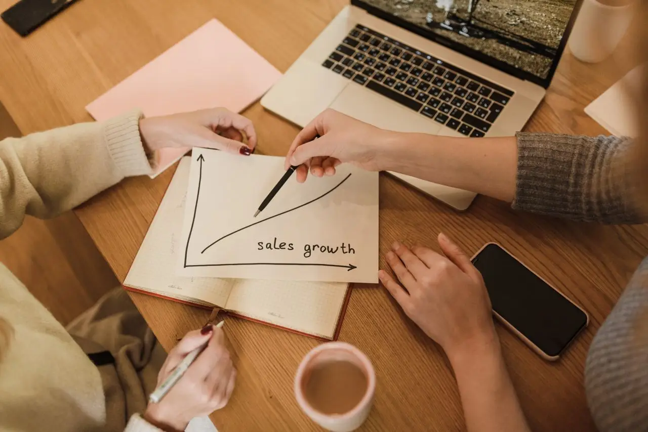 discover Two women plan sales growth with graphs and technology in an office setting.
